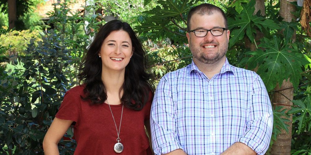 Curtin staff members, Lauren and Damian standing in front of Curtin trees, looking at camera and smiling - play video