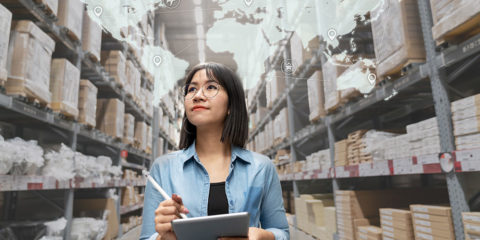 A young, Asian female walking through a warehouse, holding a clipboard