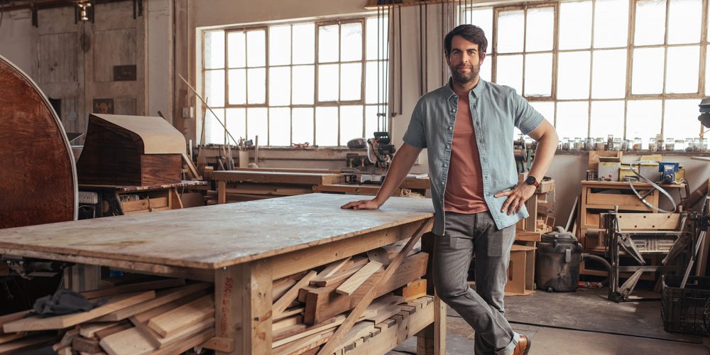 Portrait of a confident young woodworker standing next to a workbench full of wood in his carpentry workshop