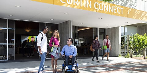 Two people standing and one man in a wheelchair waiting outside Curtin connect